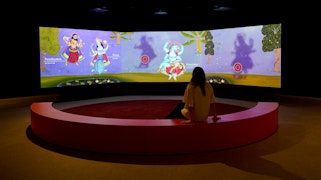 A person sitting down in front of a big screen featuring colourful artwork