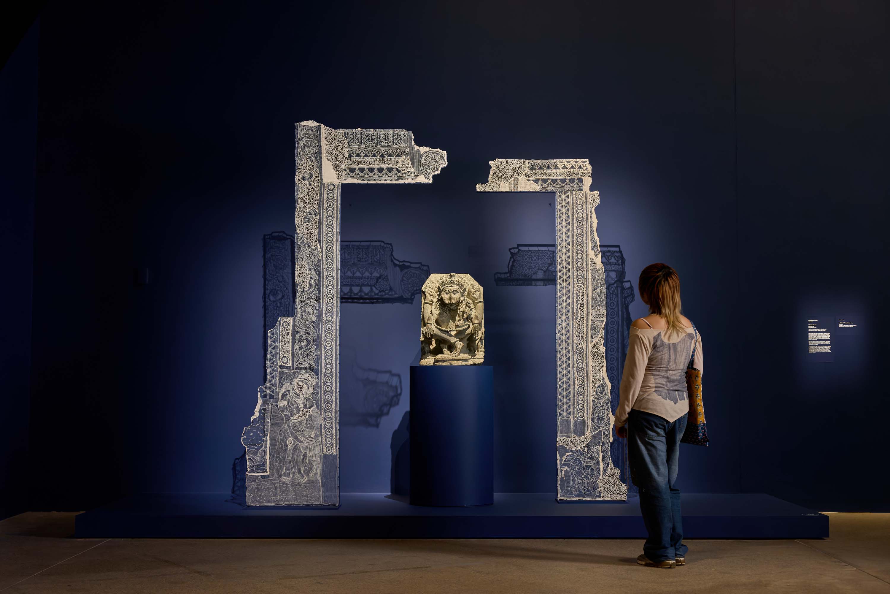 A sculpture with a fabric art installation around it, displayed against a dark blue wall.