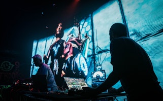Two people performing on stage in front of a large animation in the background.