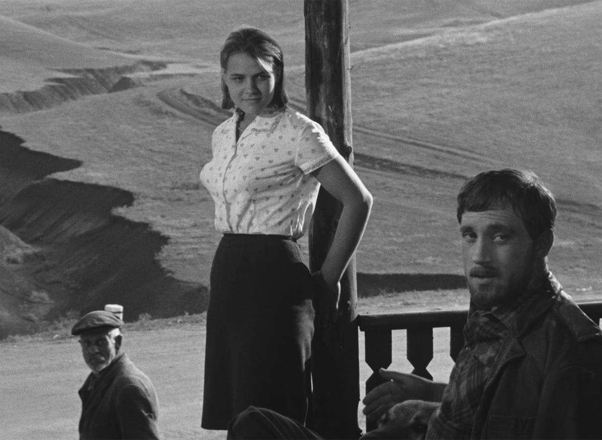 Film still of three people gazing towards the camera against a background of rolling hills