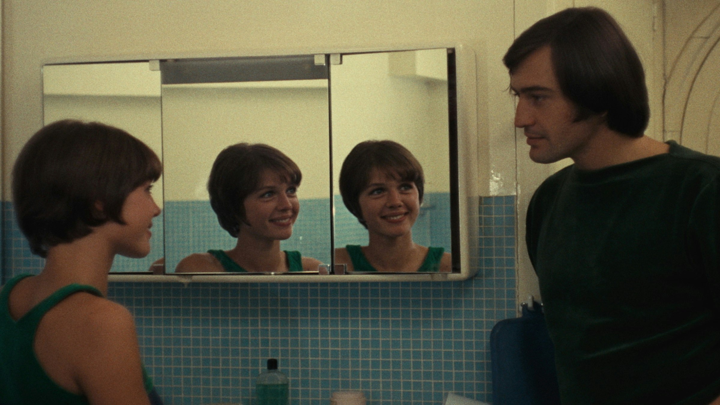 A woman smiling at a man in a bathroom with a reflection in the bathroom mirror