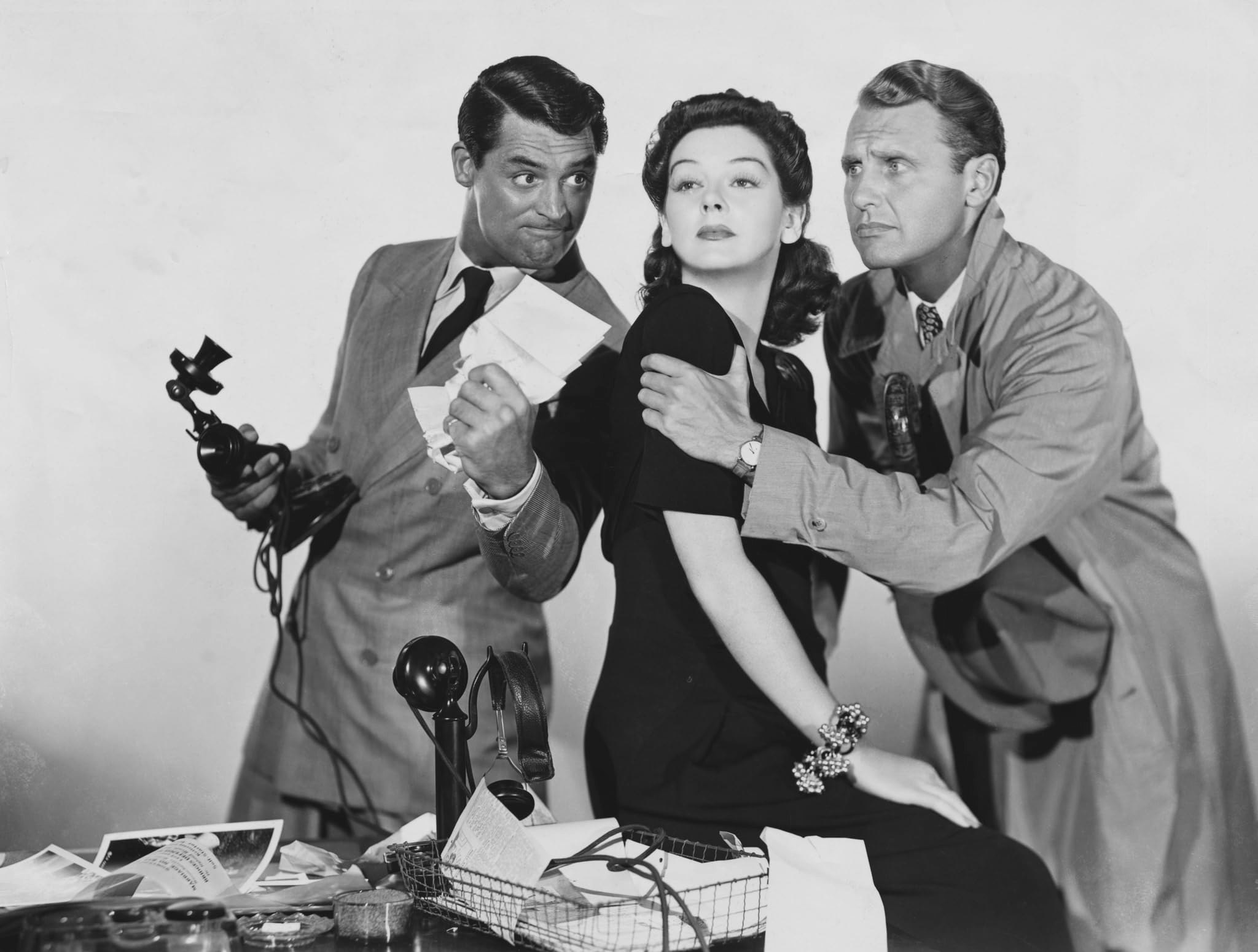 Three people standing behind a desk holding a chaotic array of office tools.