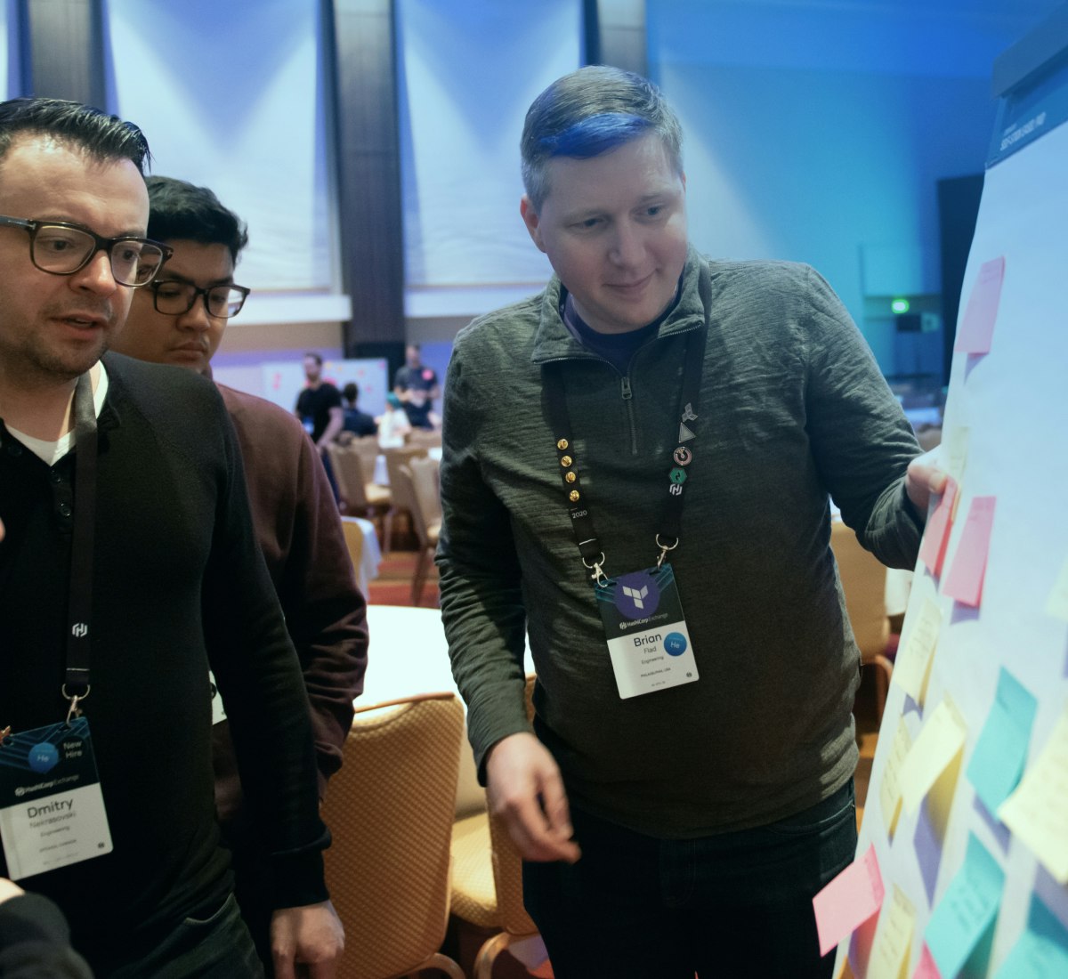 Three HashiCorp employees organizing thoughts onto a board with sticky notes.