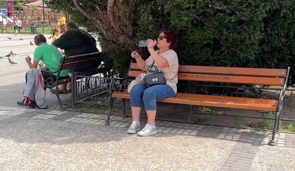 Femeie insetata care bea apă dintr-o sticlă, așezată pe o bancă