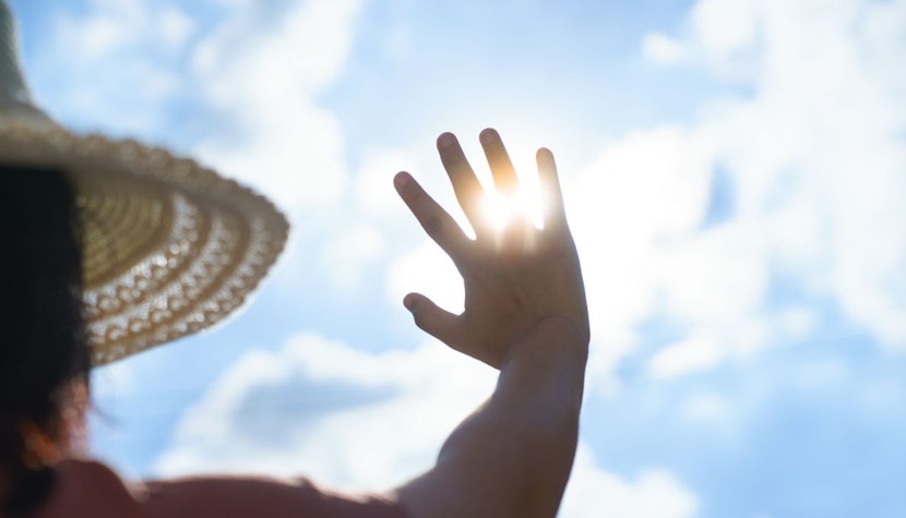 O femeie se uita la soare cu mana ridicata