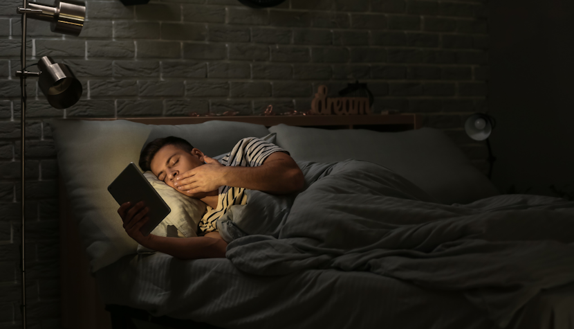 tânăr stă în pat cu tableta în mână