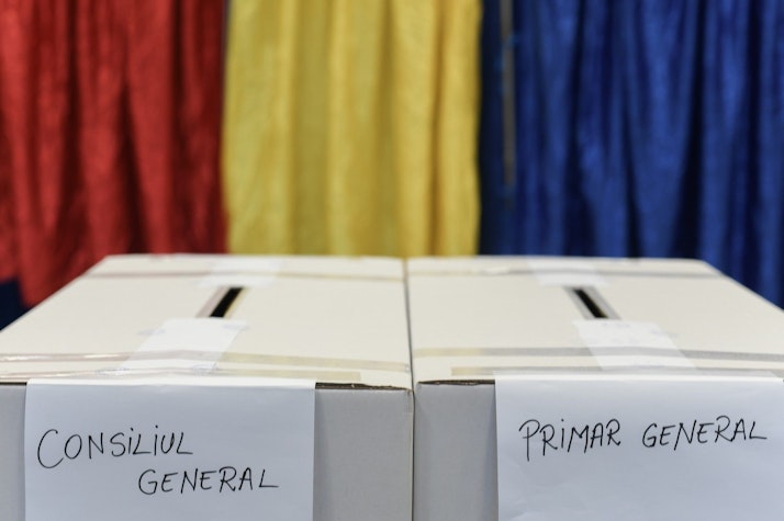 urnele de vot de la alegerile pentru consiliul general și primarul general, iar pe fundal, tricolorul