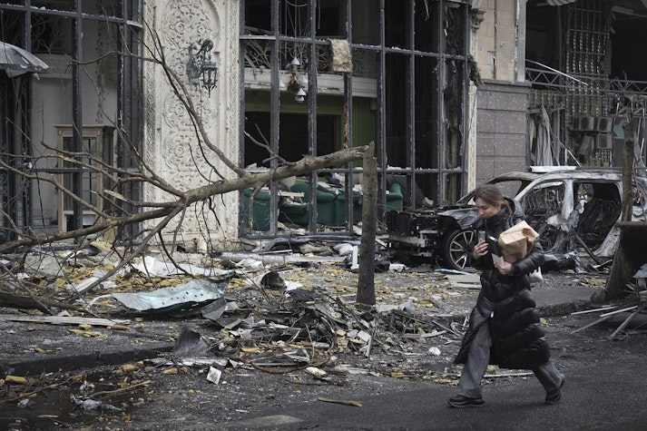 femeie trece pe langa o cladire bombardata