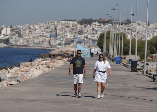Doi turiști plimbându-se, într-o localitate din Grecia
