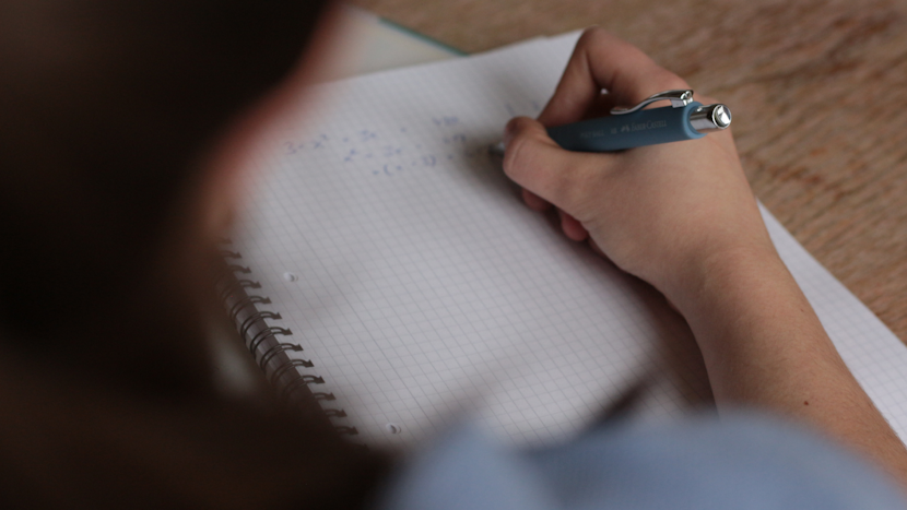 elevă care scrie o ecuație pe un caiet de matematică