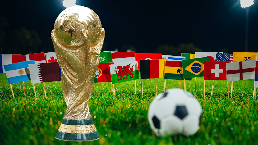 Trofeul Cupei Mondiale FIFA plasat pe gazon, înconjurat de mini-steaguri ale diferitelor țări participante și o minge de fotbal în prim-plan