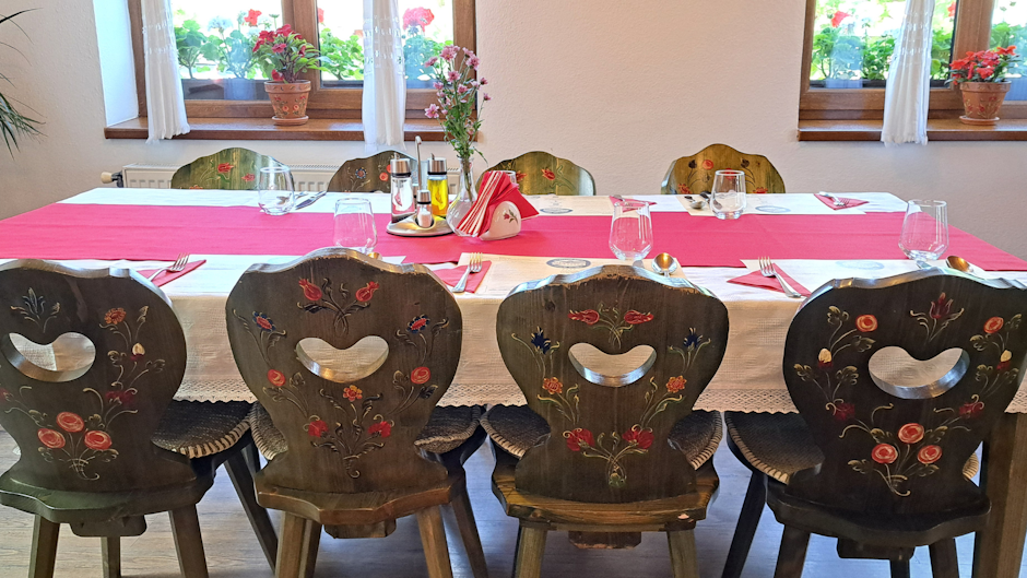 masă aranjată într-un restaurant tradițional, cu față de masă albă și roșie, scaune din lemn pictate cu motive florale