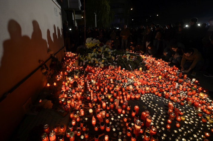 Mai multe persoane si copii depun flori si aprind candele langa clubul Colectiv