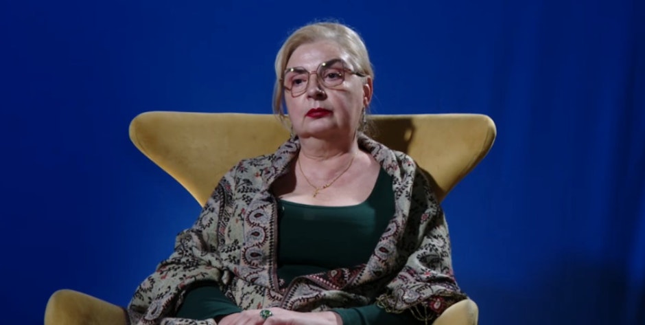 Ruxandra Geambașu, mama Ioanei Geambașu, pe un scaun galben și fundal albastru