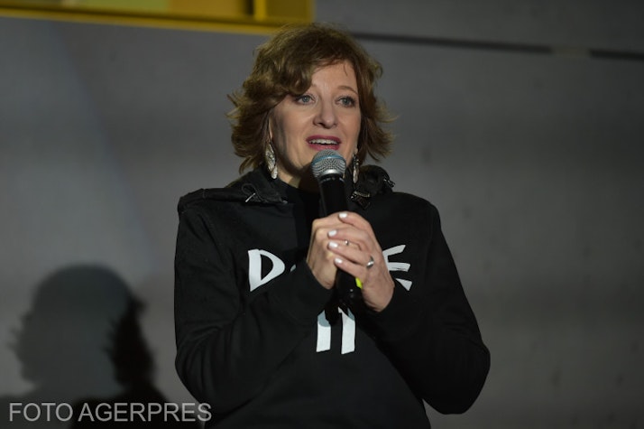 Oana Georghiu, îmbrăcată într-o haină neagră, ținând în mână un microfon