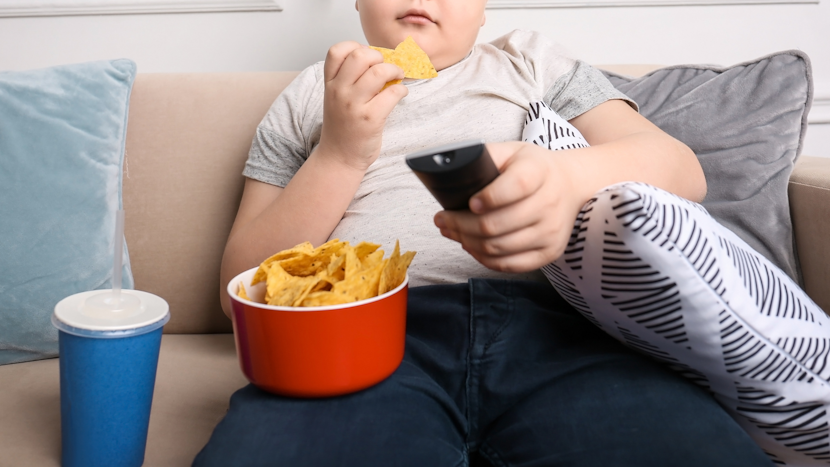 Copil care stă pe canapea și manancă nesănătos