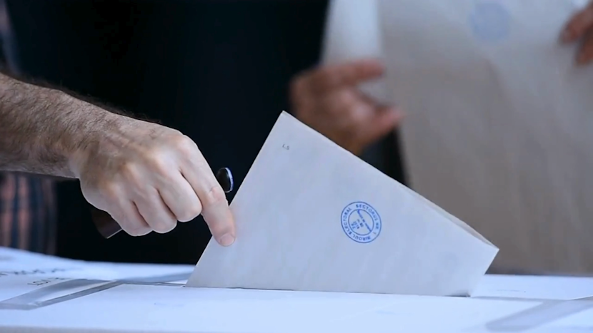 mâna unui vărbat introduce un buletin de vot într-o urnă