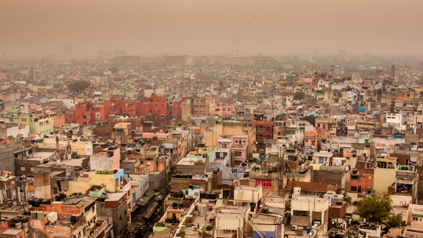 Panoramă asupra orașului Delhi acoperit de un strat dens de smog, cu clădiri colorate și cartiere aglomerate abia vizibile prin ceața poluantă.