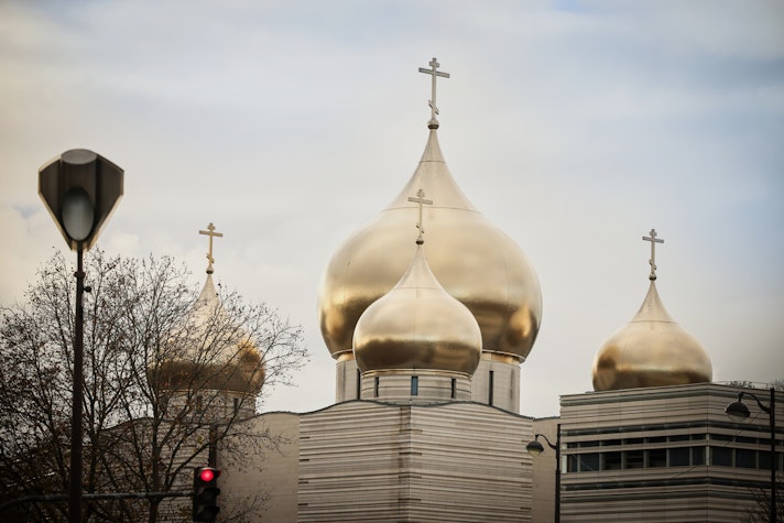 Catedrala ortodoxă rusă din Paris, cu cupole aurii în formă de ceapă și cruci ortodoxe, surprinsă într-o zi înnorată, cu siluete de copaci și un semafor în prim-plan.