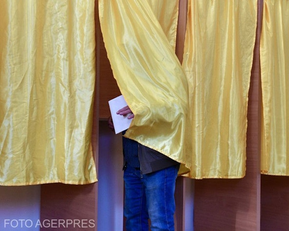 cabină de votare cu perdea galbenă, din care iese un bărbat cu un buletin de vot