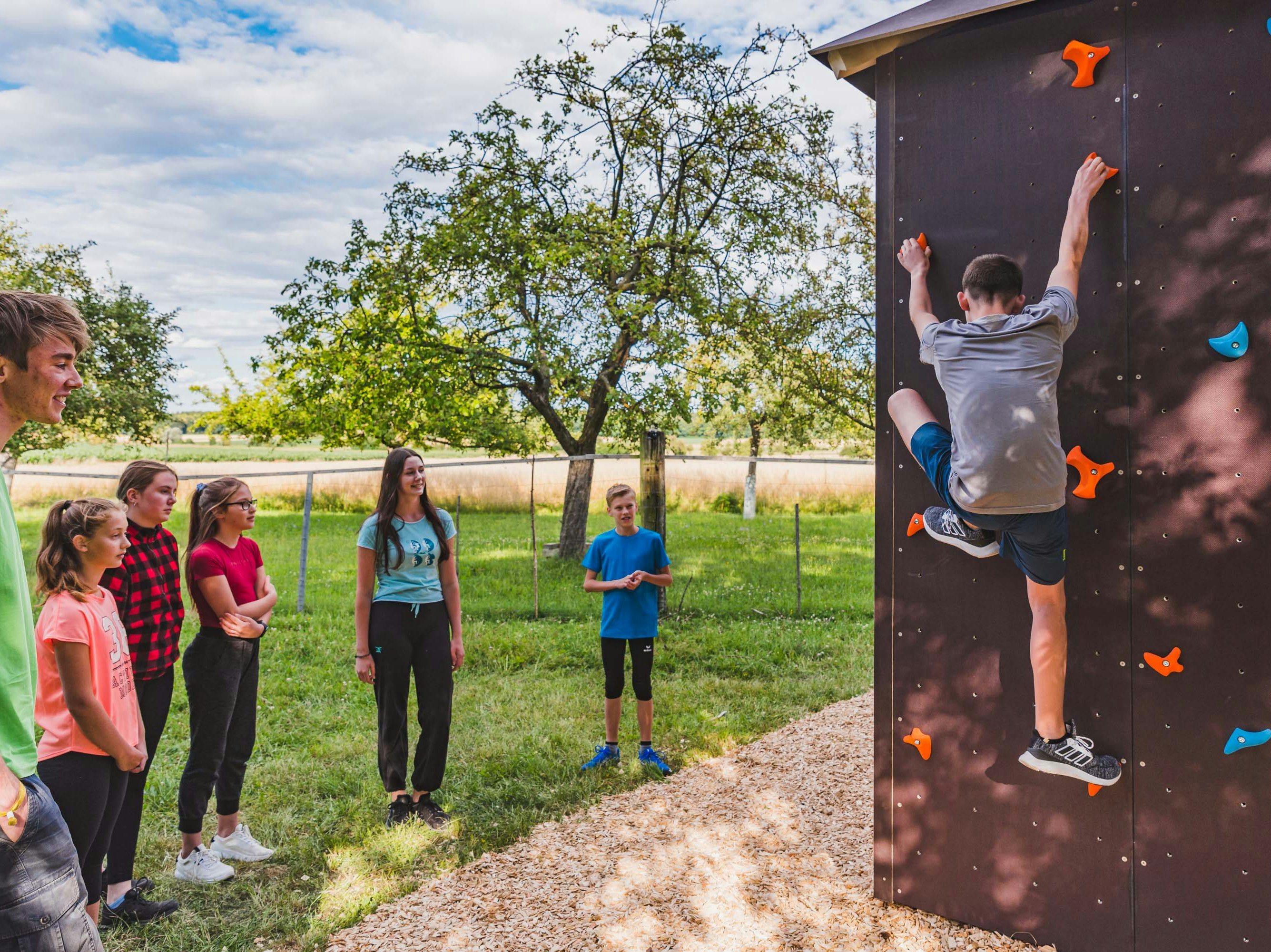 Ein junger Mensch klettern und eine Gruppe junger Menschen schaut ihm zu.
