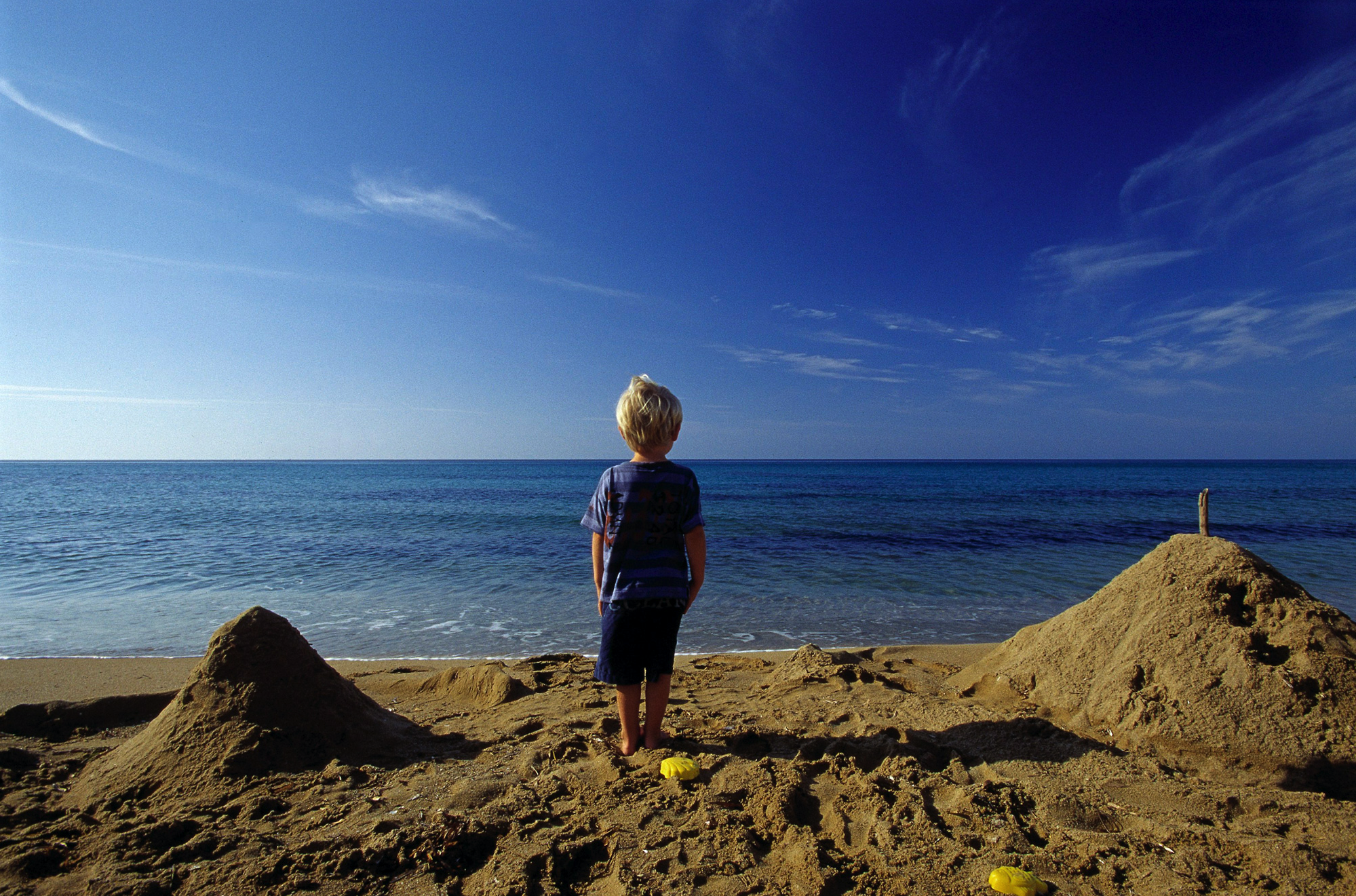 Jongetje tussen de zandkastelen op het strand kijkt naar de zee