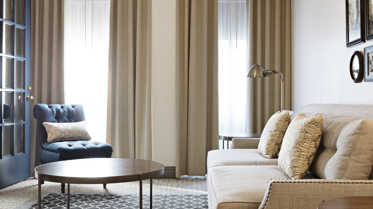 Stylish blue chair and off-white couch with light filtering through tall windows in the background