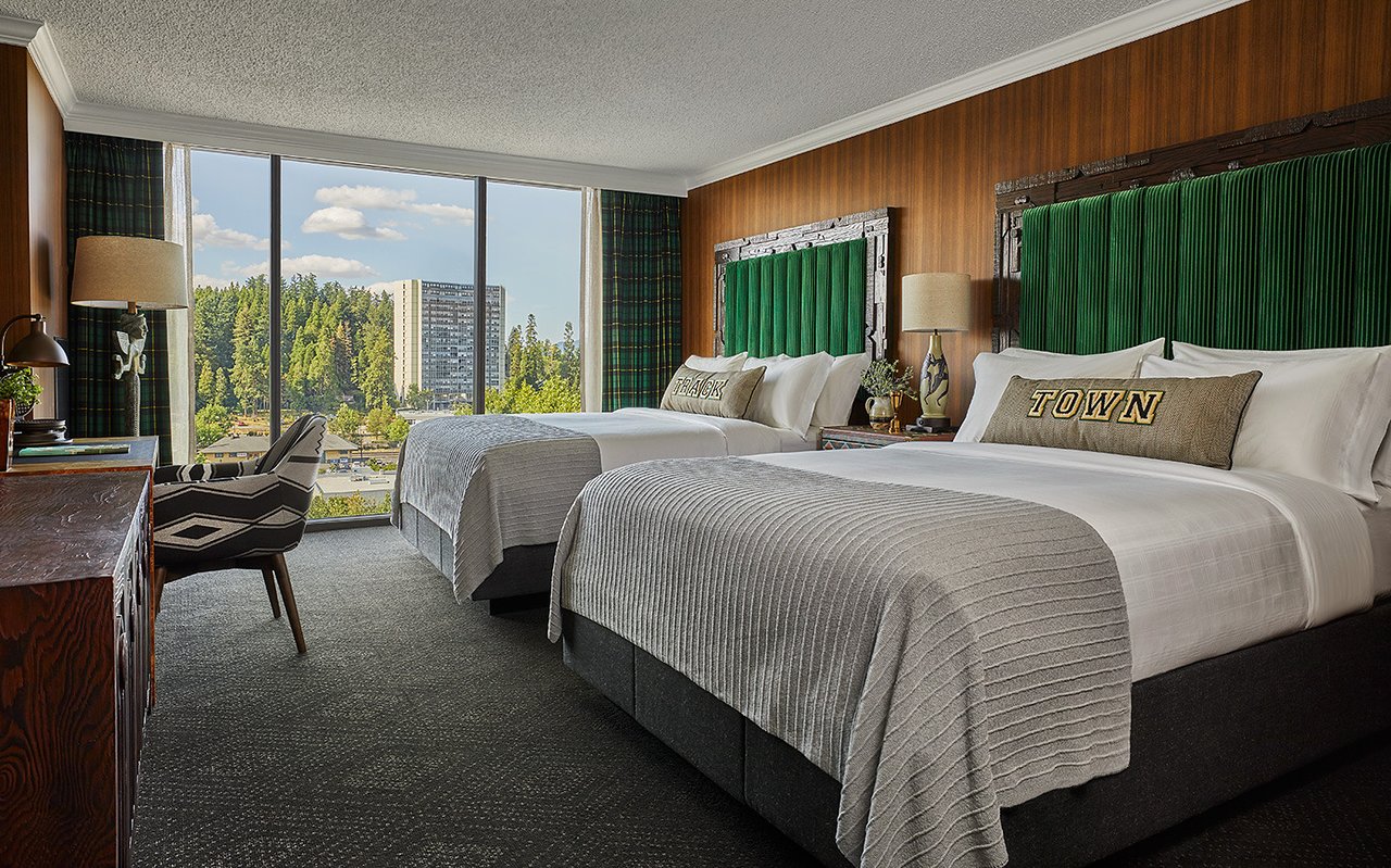 Off-the-side shot of stylish hotel suite with two beds and a beautiful view of the through the window in the background