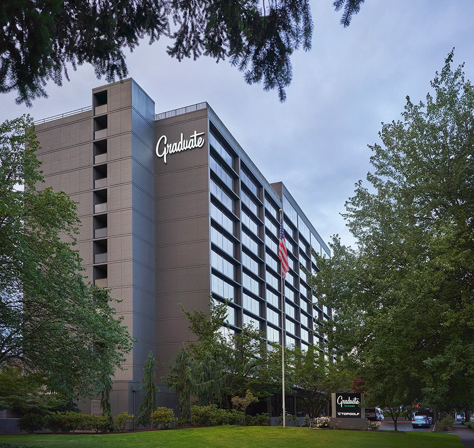 Exterior shot of hotel surrounded with foliage with stylish, cursive writing of the Graduate logo aside the building