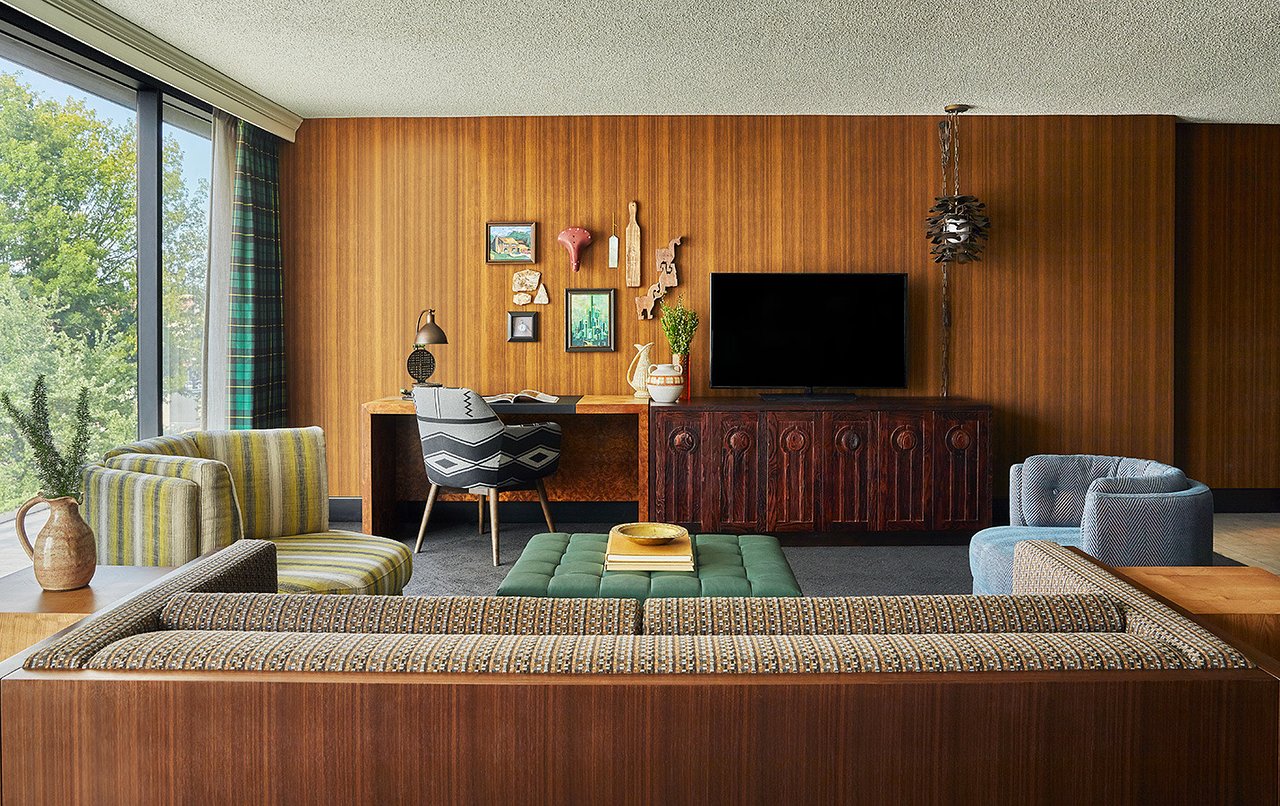 Stylish hotel suite with back of couch in foreground and wooden desk alongside TV and wooden wall