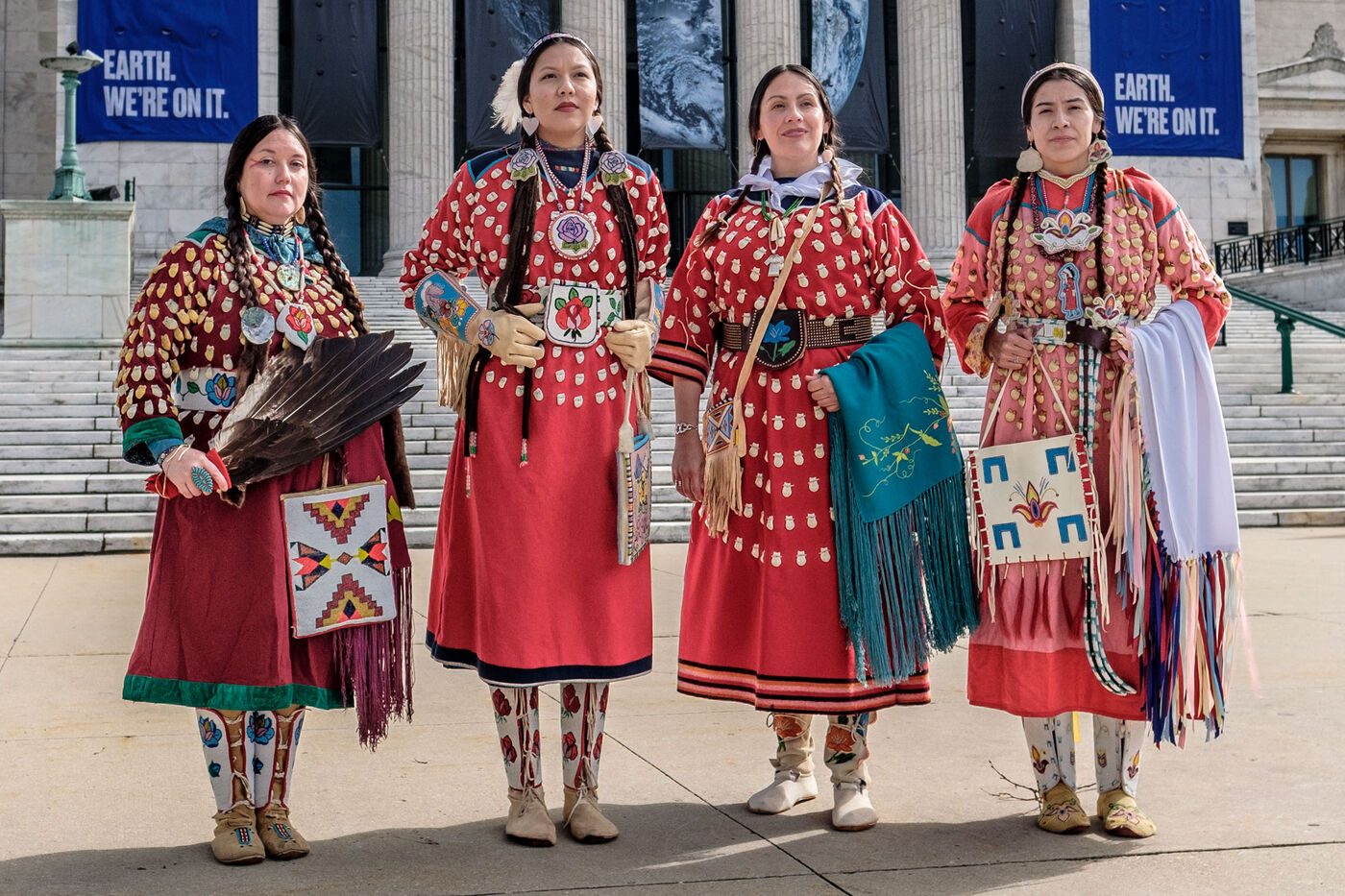 Four women dressed in Apsáalooke attire stand in front of the Field Museum. 