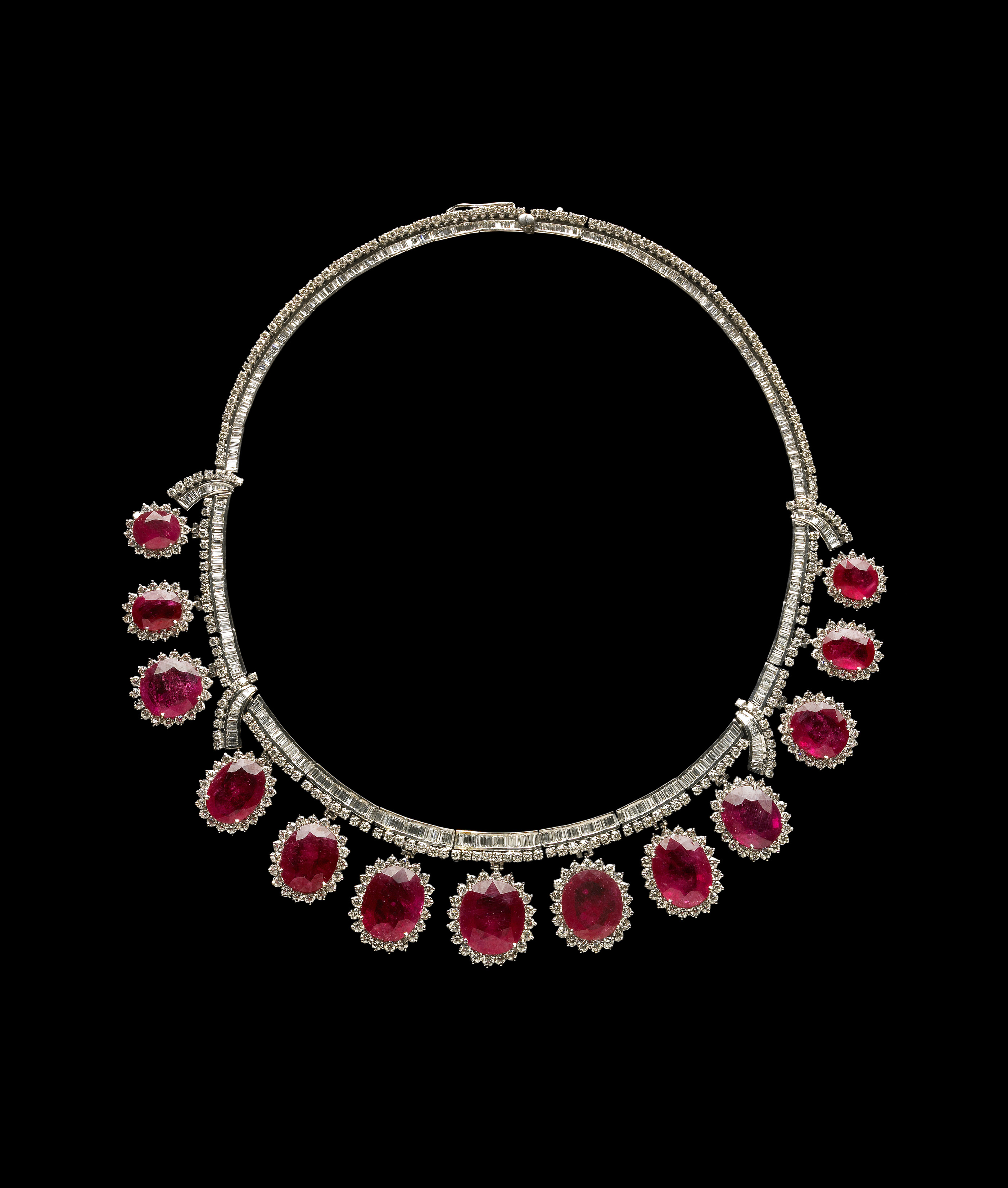 A ruby necklace, with 13 faceted oval rubies totaling 90 carats in weight, set in Platinum, hang from a collar of several hundred small baguette and round accent diamonds. Each oval ruby is surrounded by several round accent diamonds.