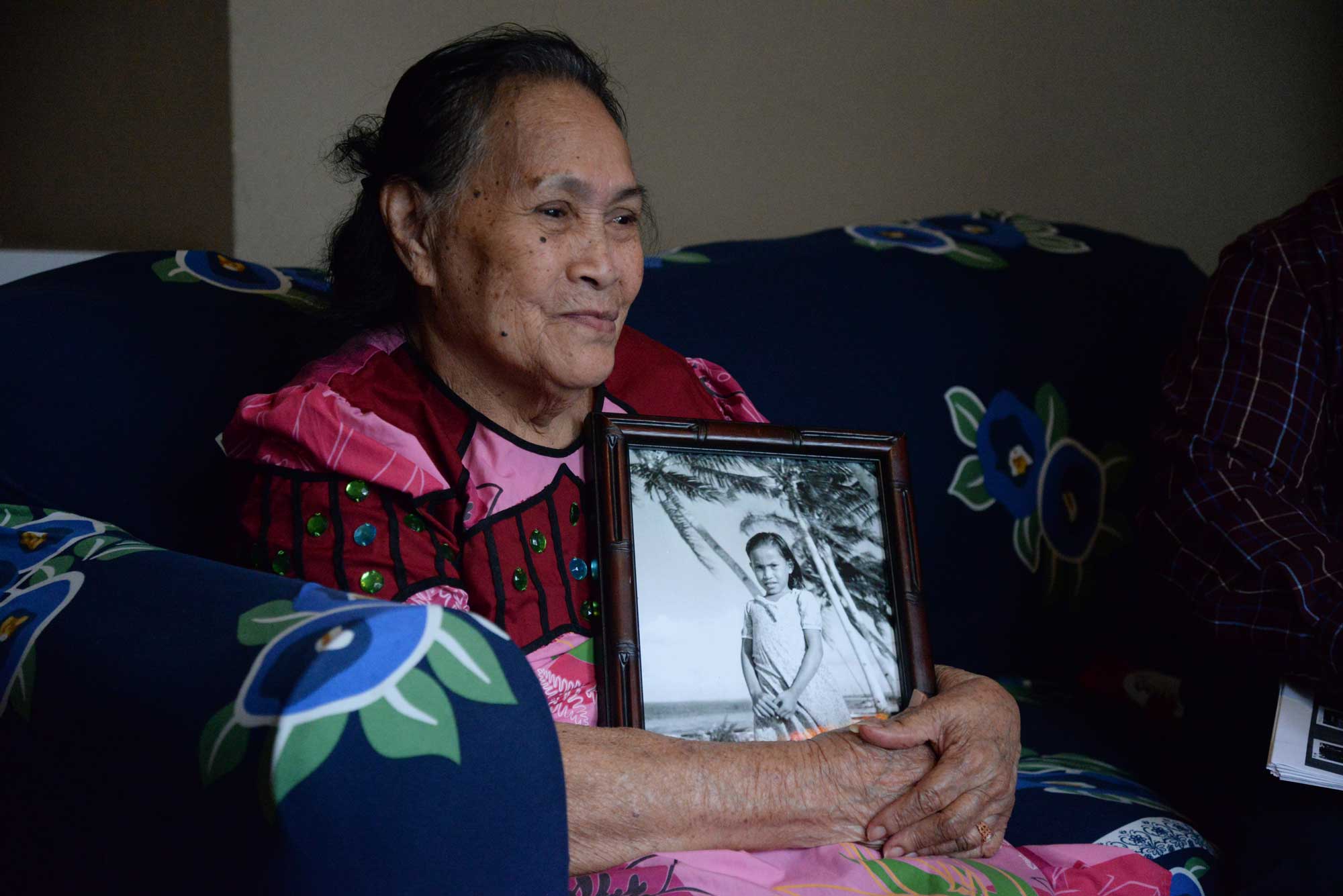 Sitting on a couch, Mojina Mote holds a framed photo of herself as a young girl.