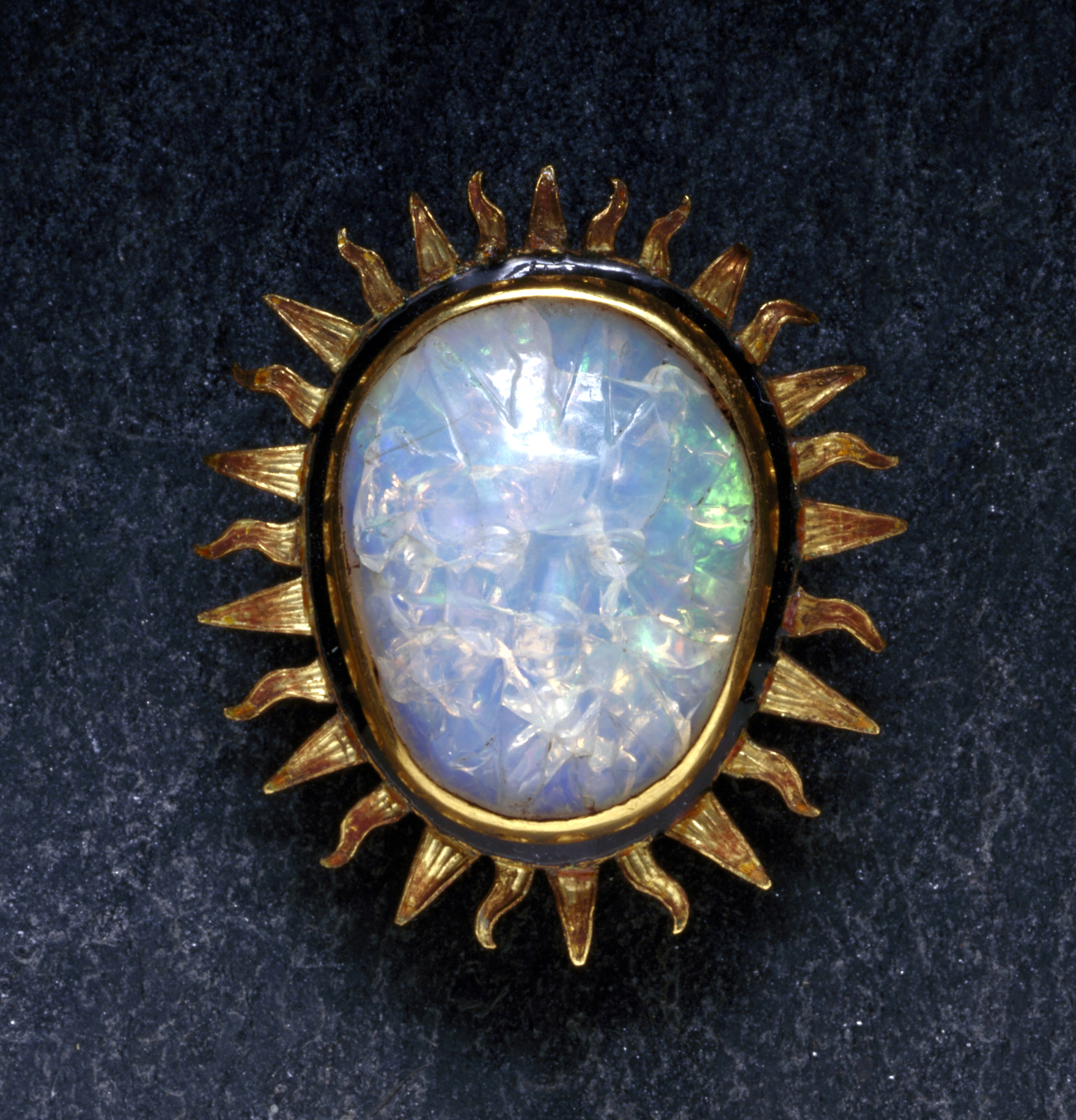 An Opal Cabochon brooch with carved face of Sun God; Its gold mounting has flame-like rays radiating out all around.