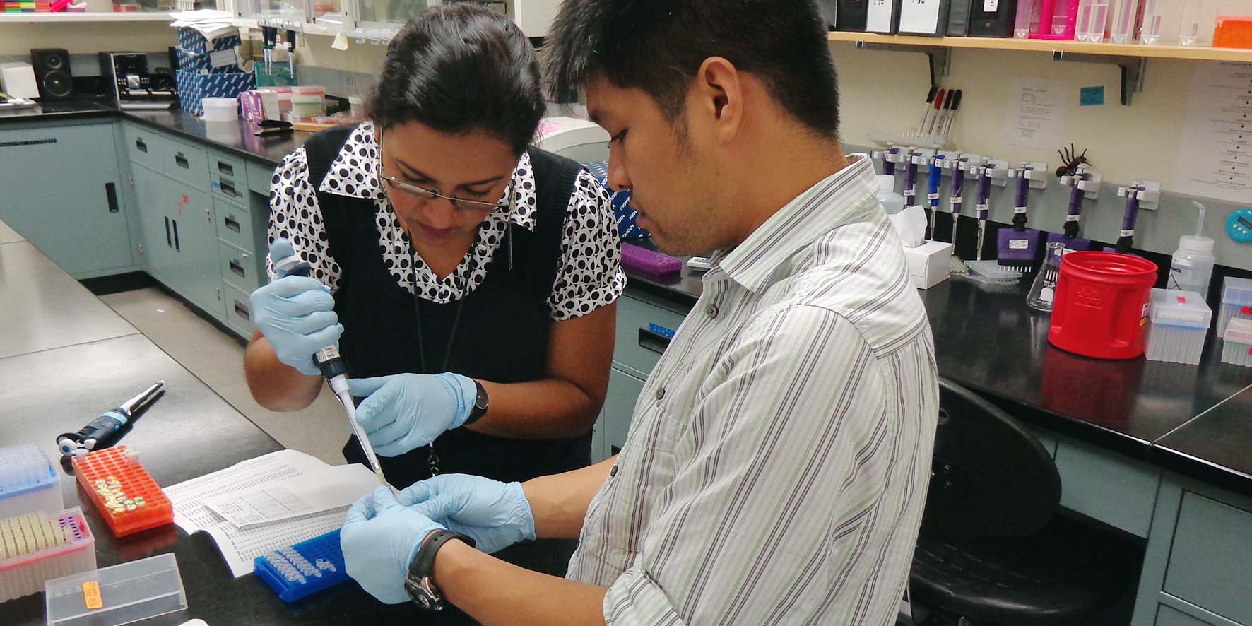 A woman and a man in a lab using a pipette