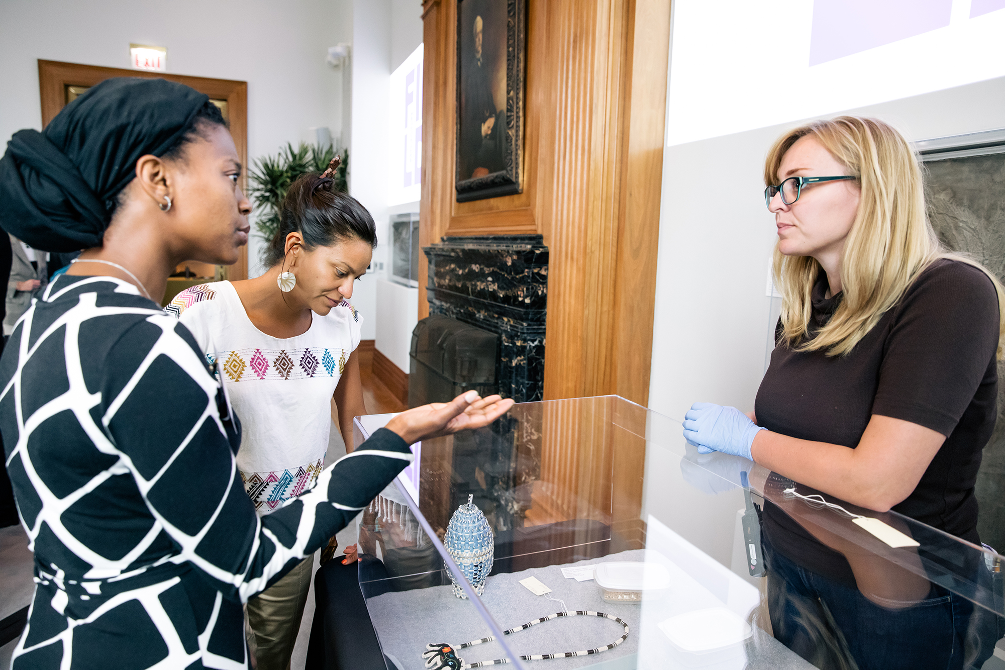 Two attendees and a museum staff member talk over a case filled with objects from the Field Museum's collections