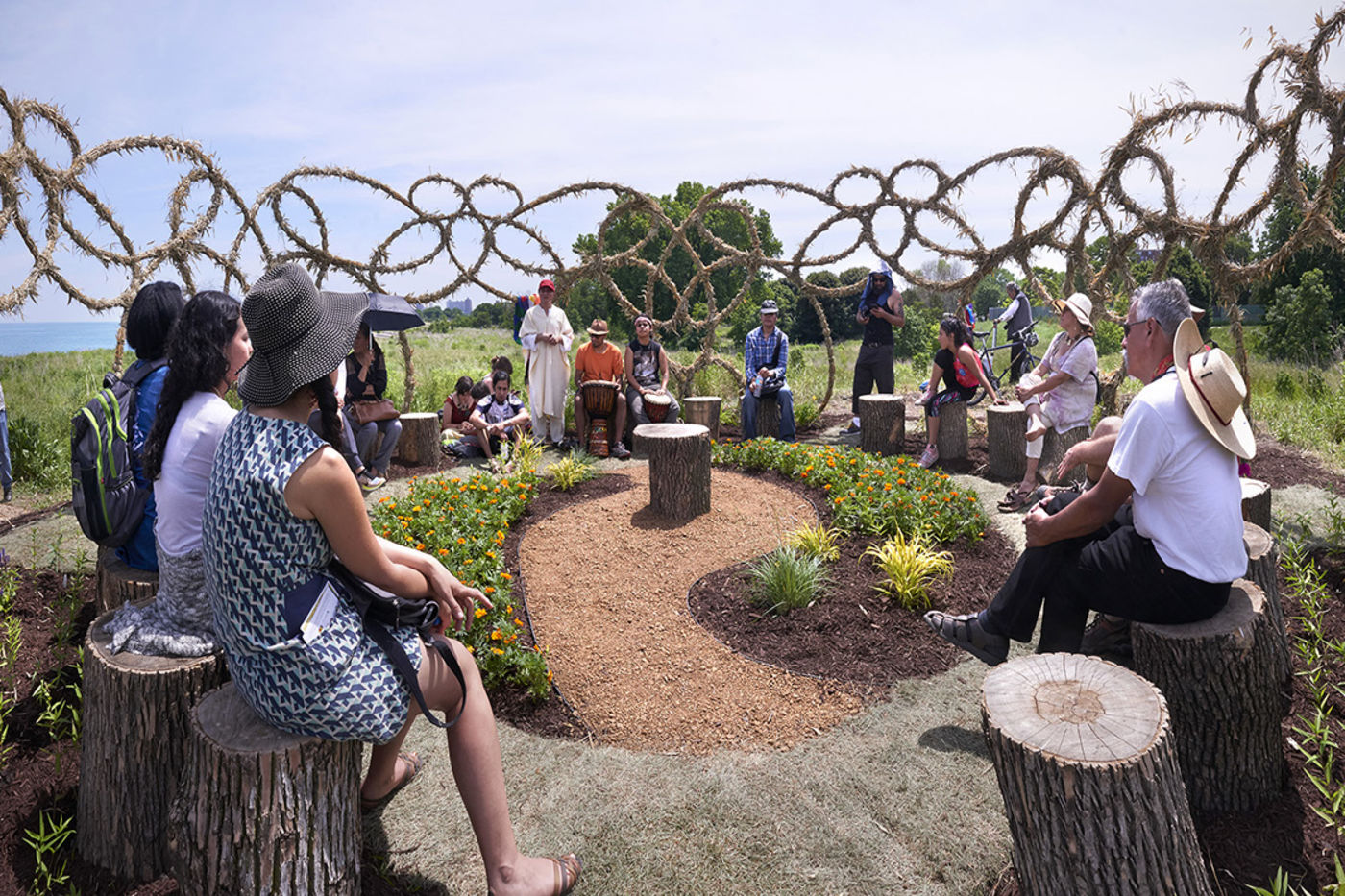 A group of people sitting in a circle on tree stumps in a park.