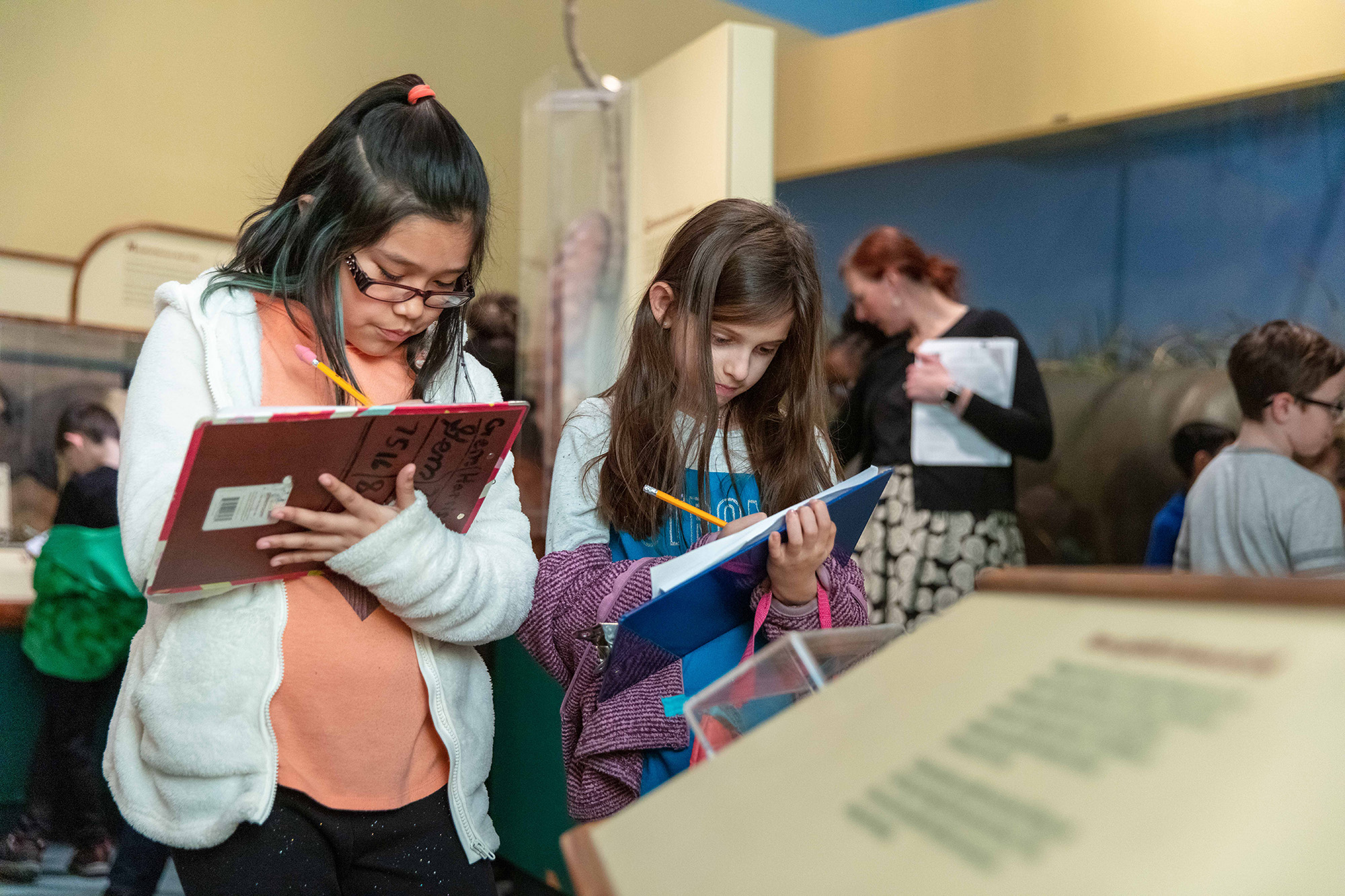 Two students write on clipboards while touring the Field Museum.