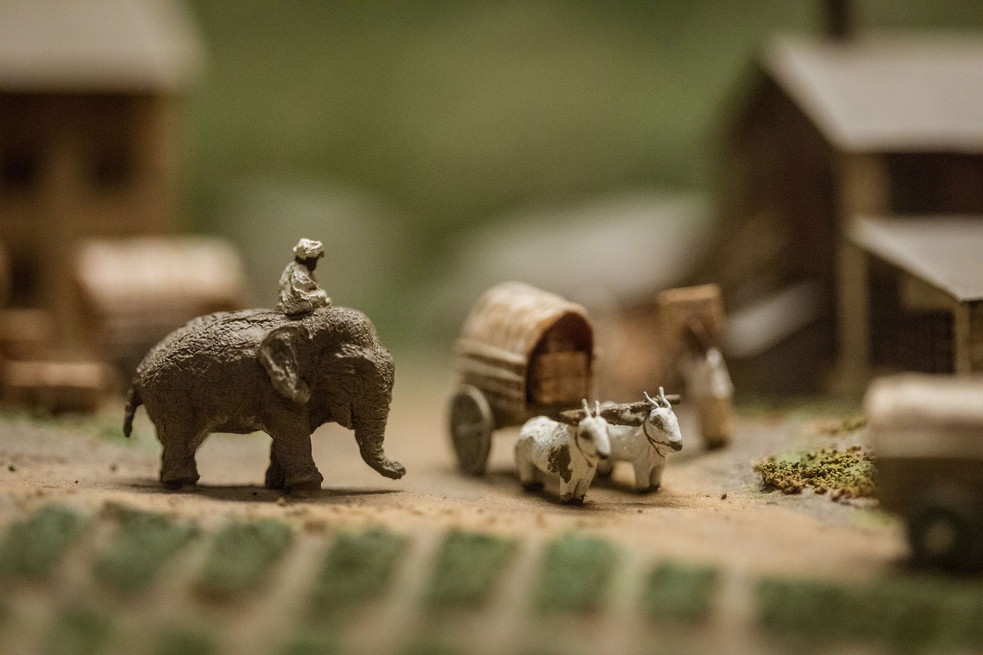 Close-up view of a diorama featuring a man riding an elephant and two goats pulling a wagon.