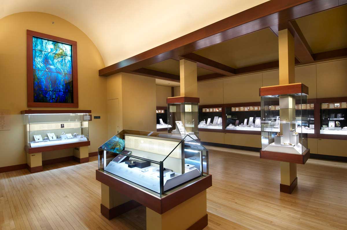 The Grainger Hall of Gems gallery at the Field Museum, including glass display cases and a blue stained glass window.