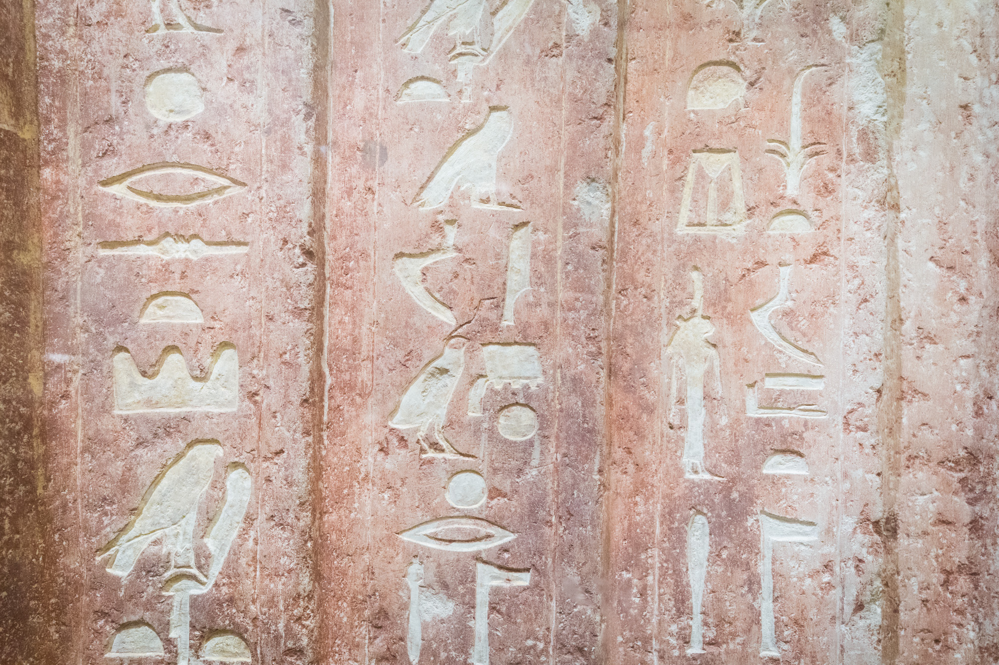 Three columns of hieroglyphs carved into the faded stone wall of a mastaba.