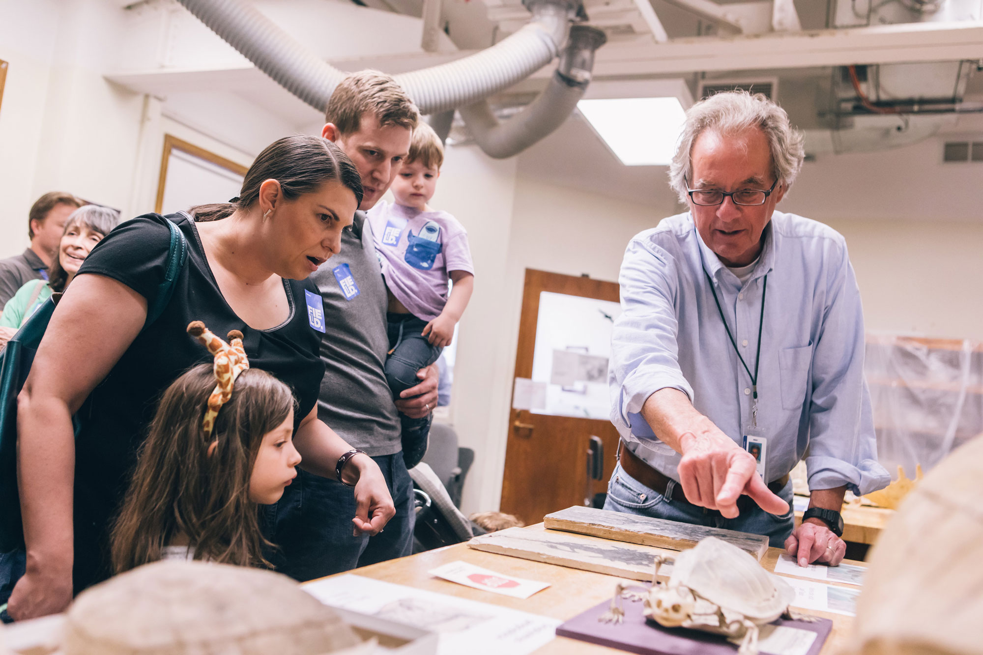 Two adults and two children listen to a staff member, who points to a specimen on display at Members’ Nights.