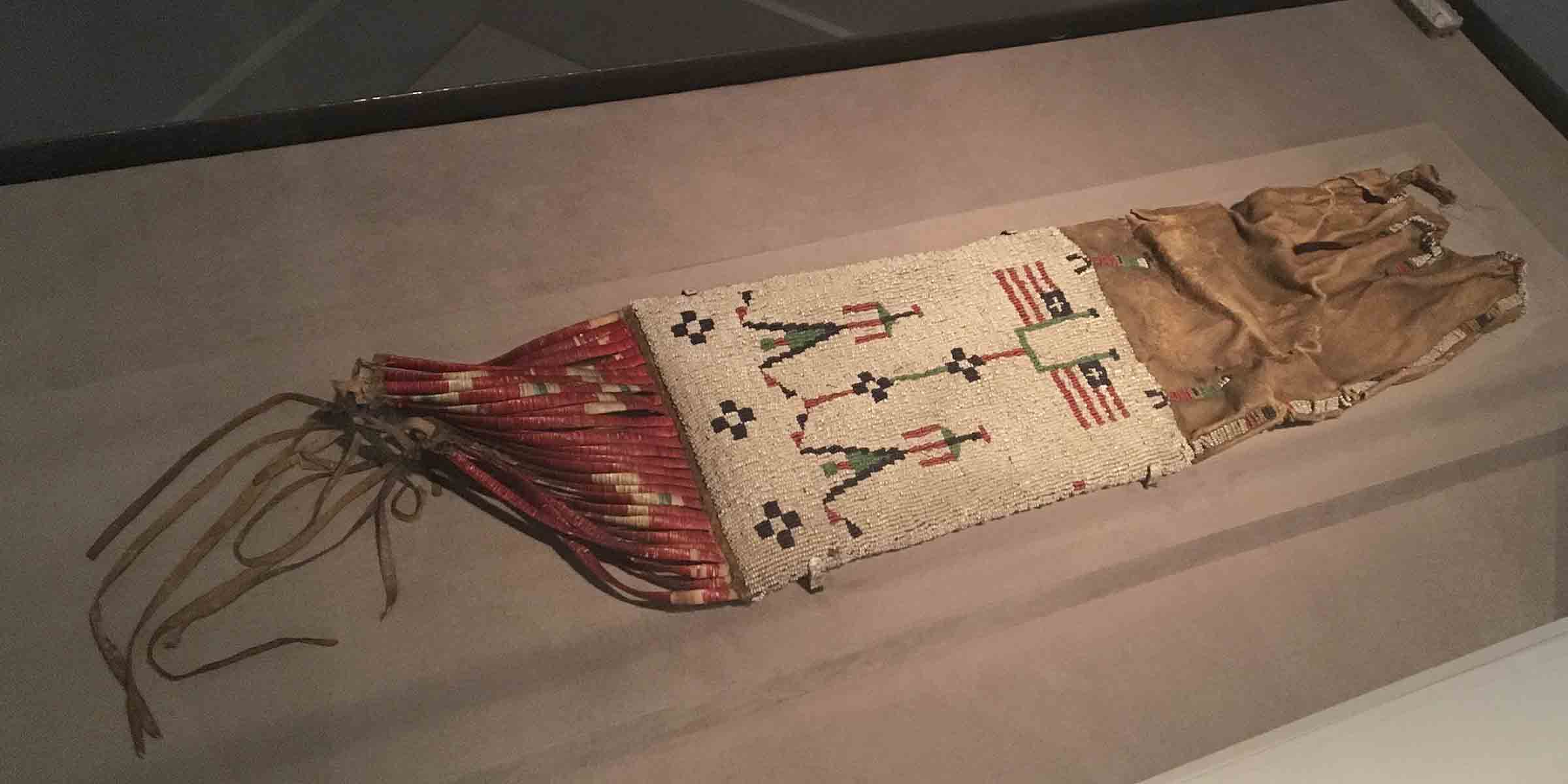 Brown, white, and red beaded bag with design of two people standing next to two flags