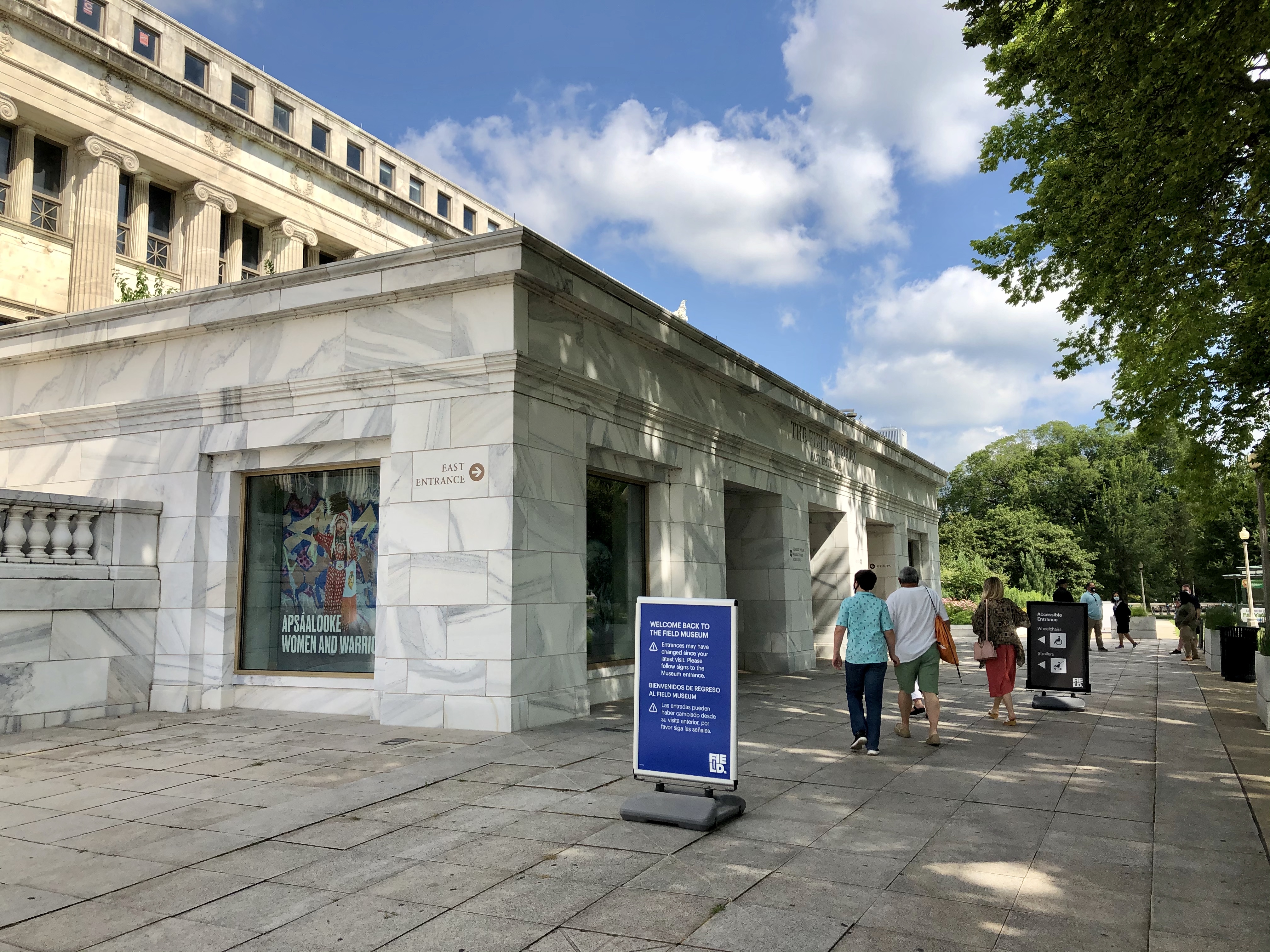 Outside the Field Museum's East entrance. Three people walk towards the door.