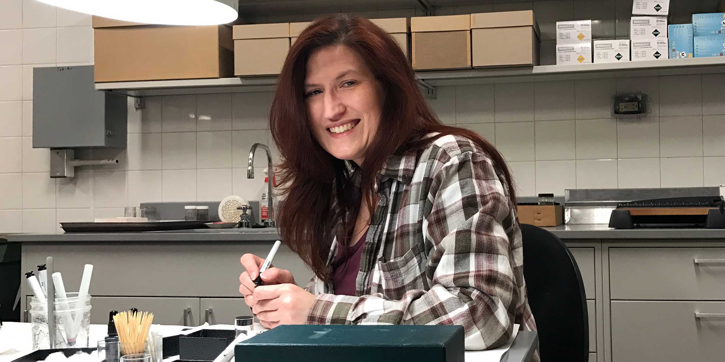 Woman sitting at a table in a lab, holding a marker and writing on something small