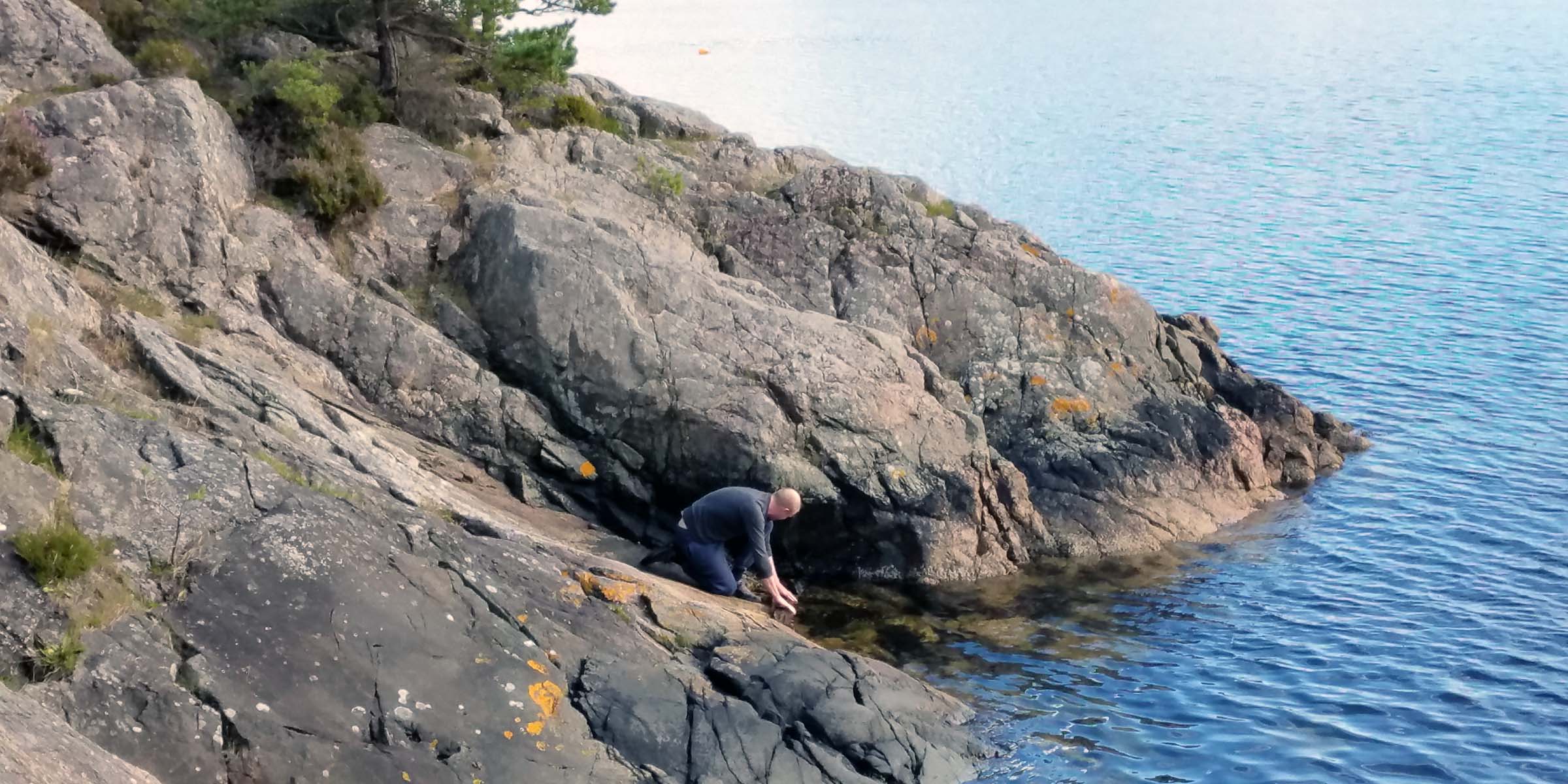 A man looking for something on a rocky coast next to bright blue water