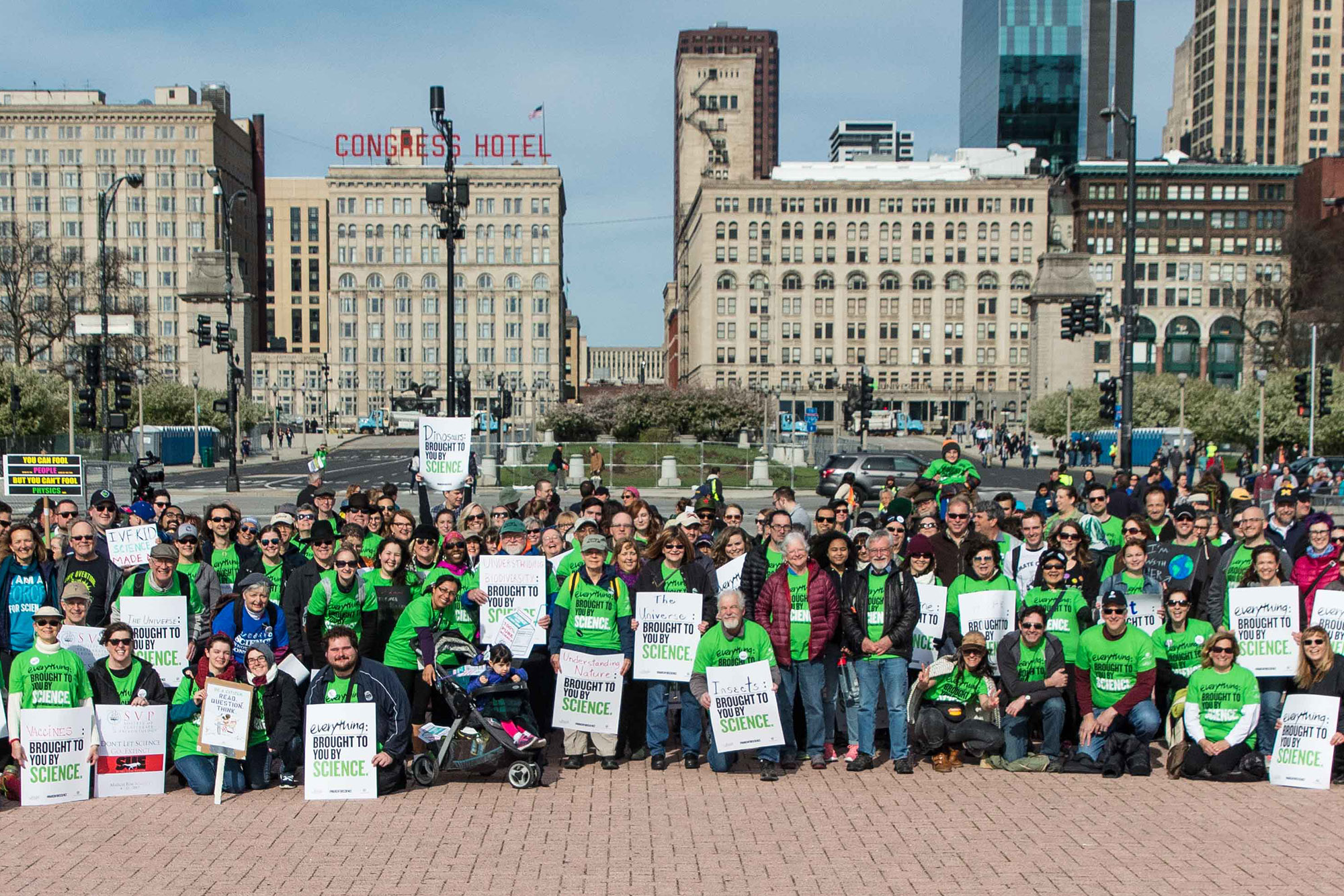 A large group of museum staff holding signs pose in Grant Park before the 2017 March for Science.