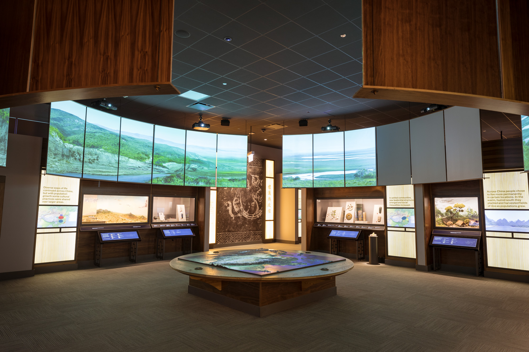 The first gallery of the Cyrus Tang Hall of China, with a map table in the foreground and a large circle of video screens above the exhibition display cases.