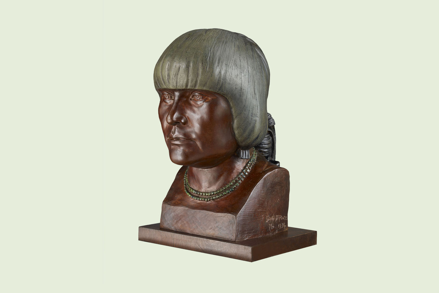 Bronze bust of Desideria Montoya Sanchez. Her eyes look straight ahead, and her short hairstyle has a grayish hue, contrasting with the brown of her face and neck, which has a greenish double-strand beaded necklace.