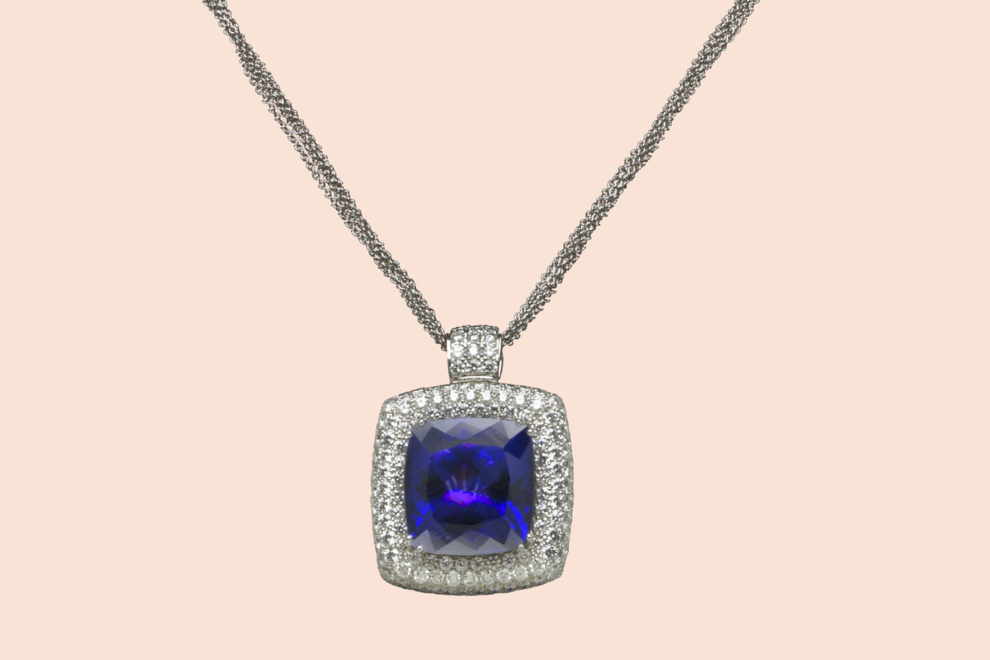 White gold necklace, featuring a large, blue gem—tanzanite. The gem is surrounded by rows of small diamonds. 